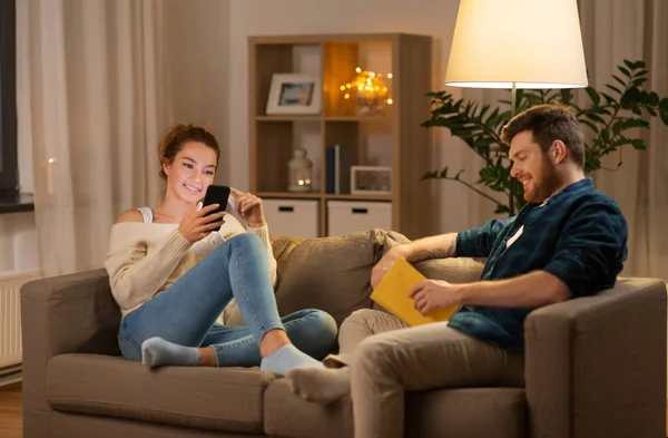 Casal com smartphone e livro em casa — Fotografia de Stock