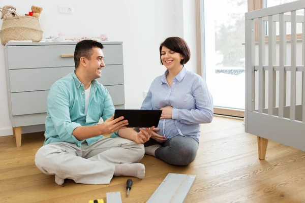 Familienpaar mit Tablet-PC baut Babybett zusammen — Stockfoto