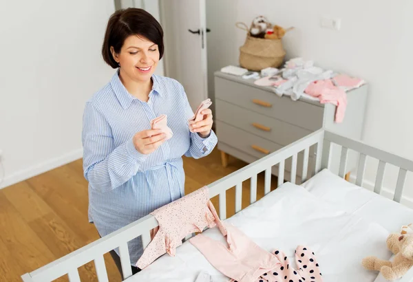 Mulher grávida feliz definir roupas de bebê em casa — Fotografia de Stock