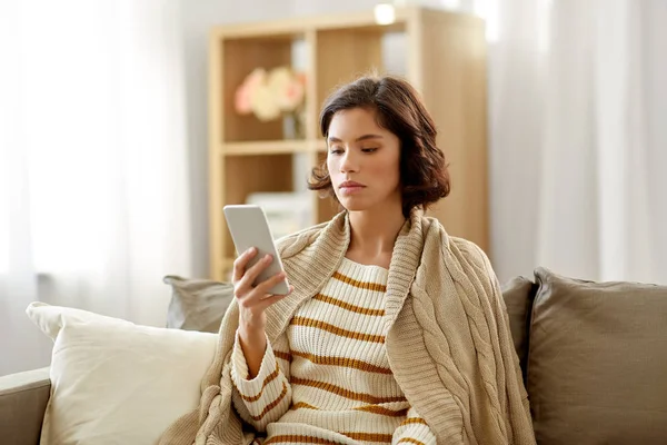 Traurige Frau in Decke nutzt Smartphone zu Hause — Stockfoto