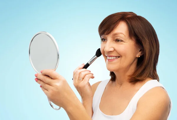 Starší žena se zrcadlem a make-upu ruměnec kartáč — Stock fotografie