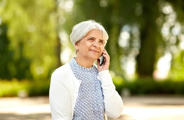 Пожилая женщина звонит на смартфон в летнем парке — стоковое фото