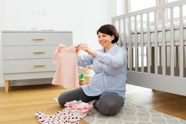 Mulher grávida feliz definir roupas de bebê em casa — Fotografia de Stock