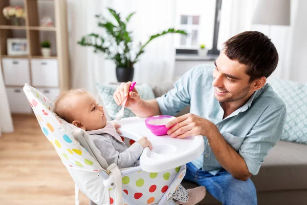 Vater füttert glückliches Baby zu Hause im Hochstuhl — Stockfoto