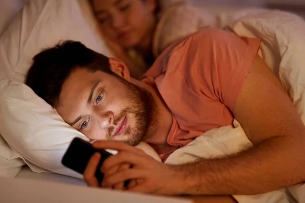 Hombre usando el teléfono inteligente mientras su novia está durmiendo —  Fotos de Stock