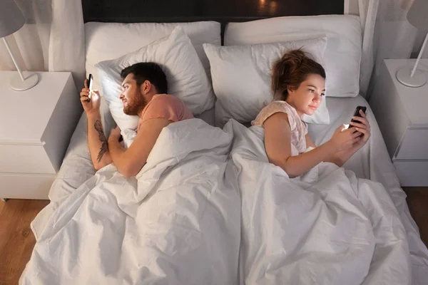 Пара с помощью смартфонов в постели ночью — стоковое фото