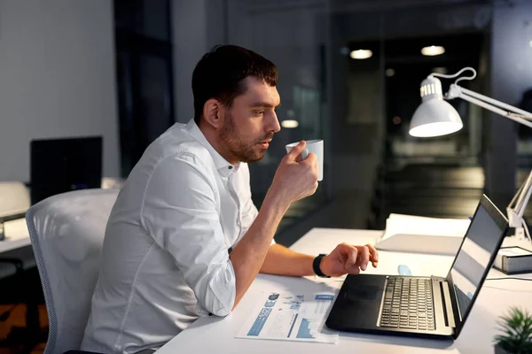 Бизнесмен с кофе и ноутбуком в ночном офисе — стоковое фото