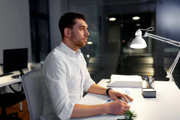 Businessman sitting at table at night office — Stock Photo, Image