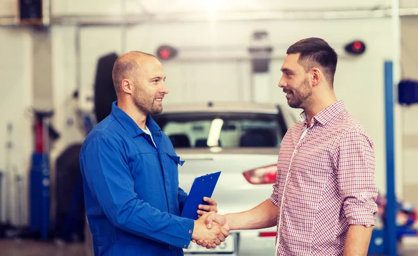 Auto mechanic and man shaking hands at car shop — Stock Photo, Image