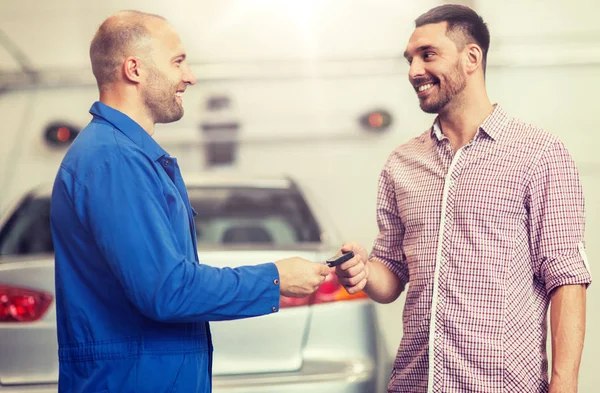 Auto mechanic giving key to man at car shop — Stock Photo, Image