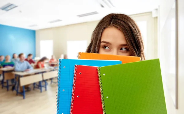 Estudiante chica escondida detrás de cuadernos en la escuela — Foto de Stock