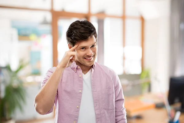 Sorridente homem apontando dedo para a cabeça no escritório — Fotografia de Stock
