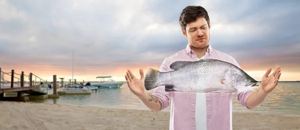 Jovem descontente mostrando tamanho de peixe na praia — Fotografia de Stock