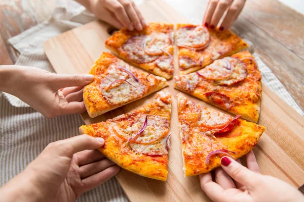 Close up of hands sharing pizza on wooden table — Stock Photo, Image