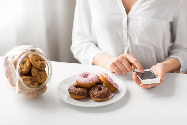 Close up de mulher com smartphone e donuts — Fotografia de Stock