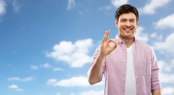 Lächelnder junger Mann zeigt Handzeichen über dem Himmel — Stockfoto