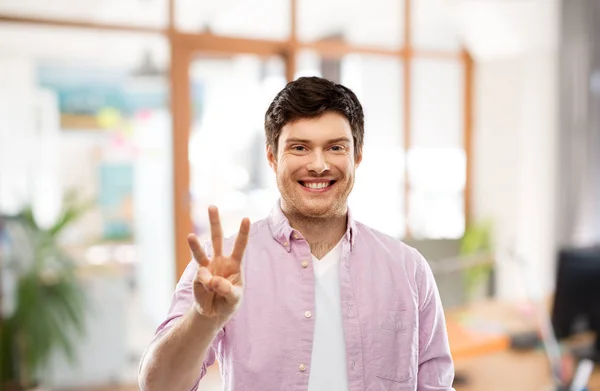Молодий чоловік показує три пальці над офісною кімнатою — стокове фото
