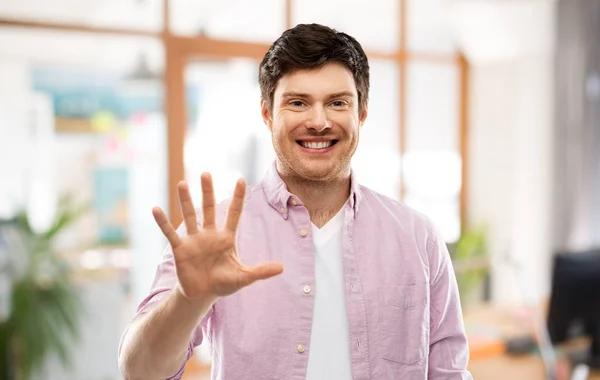 Junger Mann zeigt fünf Finger über Bürozimmer — Stockfoto