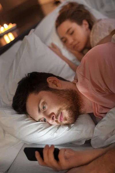 Мужчина использует смартфон, пока подруга спит — стоковое фото