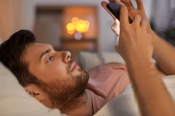 Jovem com smartphone na cama à noite — Fotografia de Stock