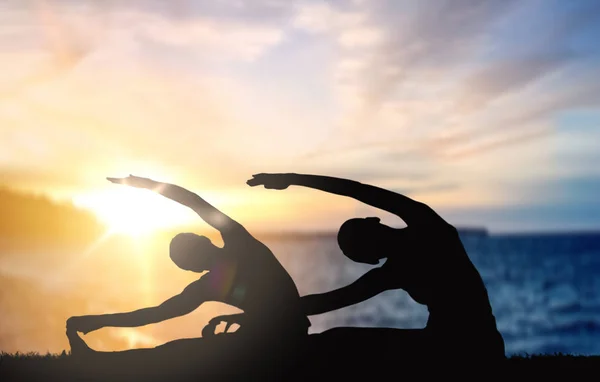 Pareja haciendo yoga sobre puesta de sol mar fondo — Foto de Stock