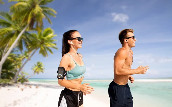 Par med telefoner och armband som löper på stranden — Stockfoto