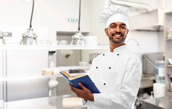 Felice chef indiano con libro di cucina in cucina — Foto Stock