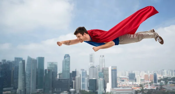 Man in red superhero cape flying in air over city — Stock Photo, Image