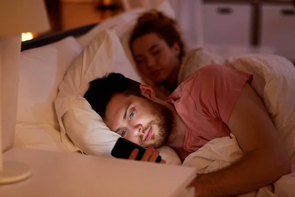Hombre usando el teléfono inteligente mientras su novia está durmiendo — Foto de Stock