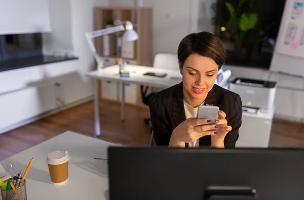 Business woman using smartphone at night office — стоковое фото