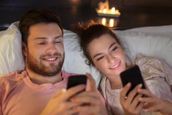 Pareja feliz usando teléfonos inteligentes en la cama por la noche Fotos de stock