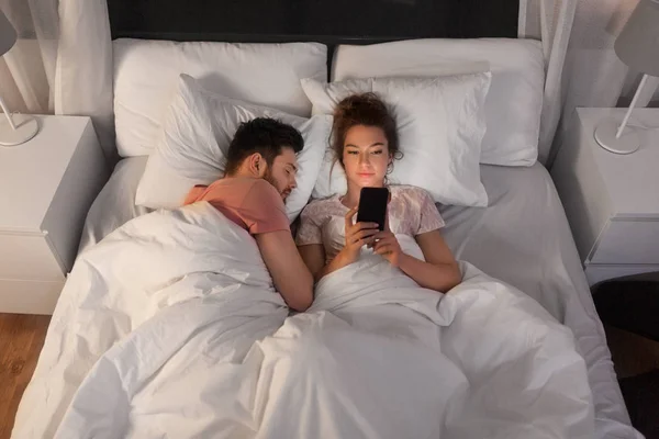 Mulher usando smartphone enquanto namorado está dormindo Fotos De Bancos De Imagens Sem Royalties