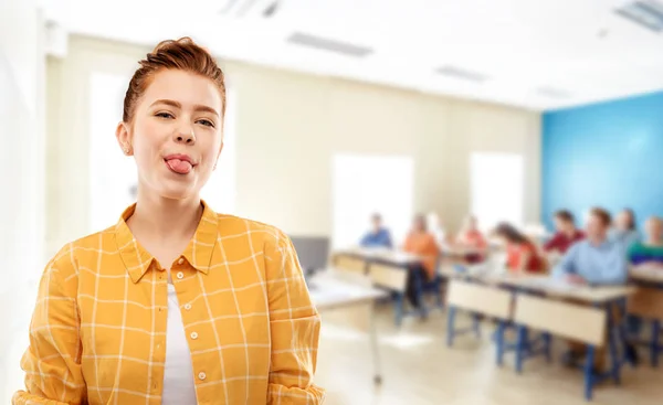 Rojo pelo estudiante chica mostrando lengua en la escuela — Foto de Stock