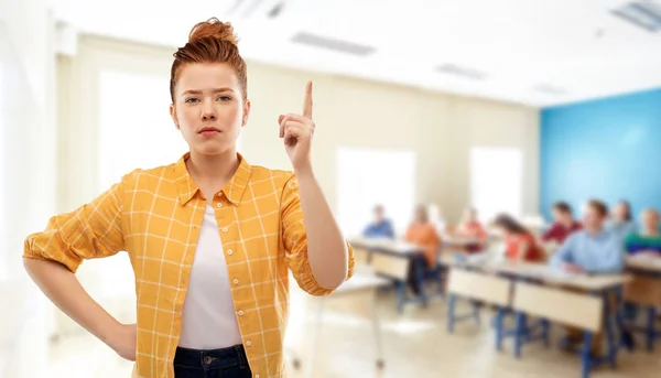 Рыжая студентка с поднятым пальцем в школе — стоковое фото