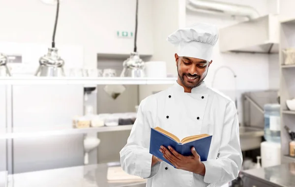 Chef indiano feliz lendo livro de receitas na cozinha — Fotografia de Stock