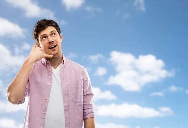 Joven mostrando el gesto de llamada telefónica sobre el cielo azul —  Fotos de Stock