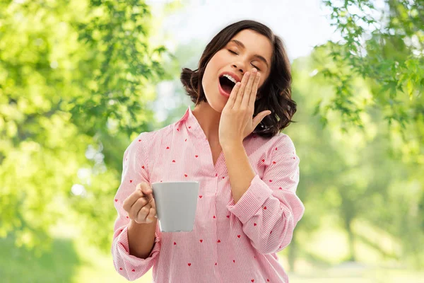 Happy yawning young woman in pajama with coffee — Stock Photo, Image