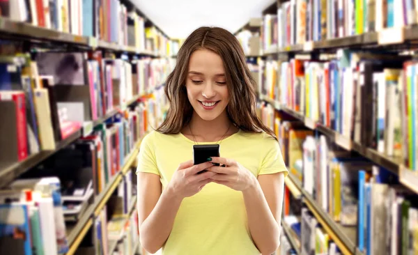 Teenage student girl using smartphone at library — Stock Photo, Image