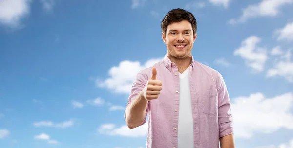 Glücklicher junger Mann zeigt Daumen hoch über blauem Himmel — Stockfoto