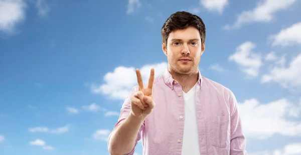 Young man showing two fingers over sky — Stock Photo, Image