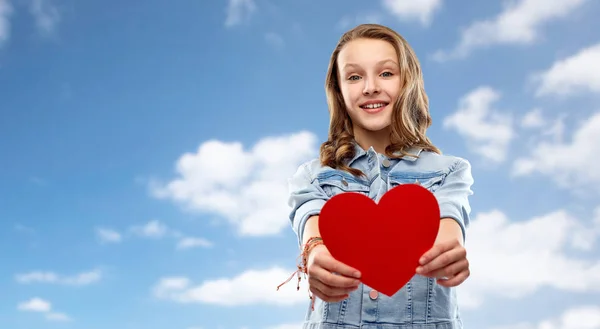 Smiling teenage girl with red heart over sky — Stock Photo, Image