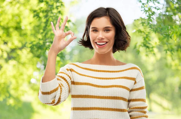 Glücklich lächelnde Frau in gestreiftem Pullover zeigt ok — Stockfoto