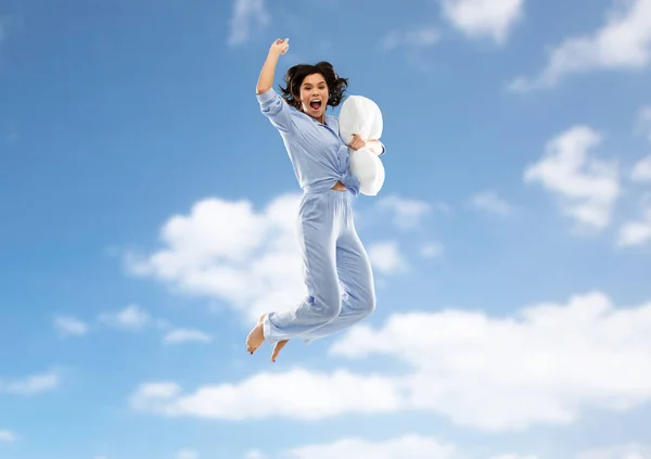 Lycklig kvinna i pyjamas hoppning med kudde över himlen — Stockfoto
