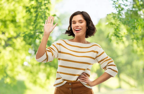 Lächelnde Frau in gestreiftem Pullover, winkende Hand — Stockfoto