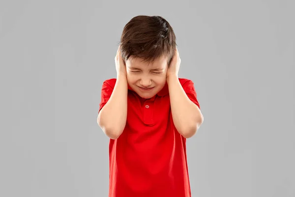 Niño estresado en camiseta roja cerrando las orejas por las manos —  Fotos de Stock