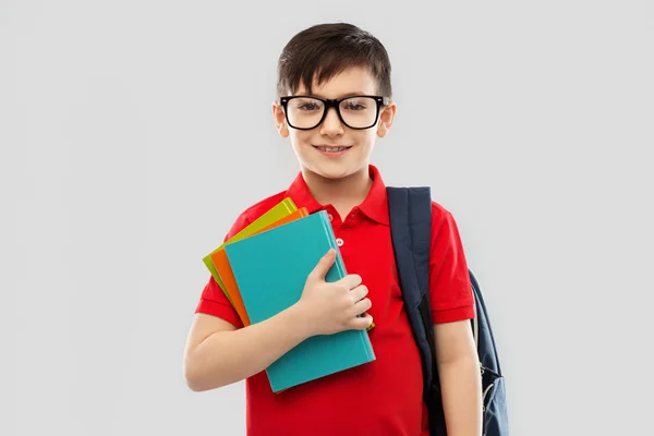 Leende skolpojke i glasögon med böcker och väska — Stockfoto