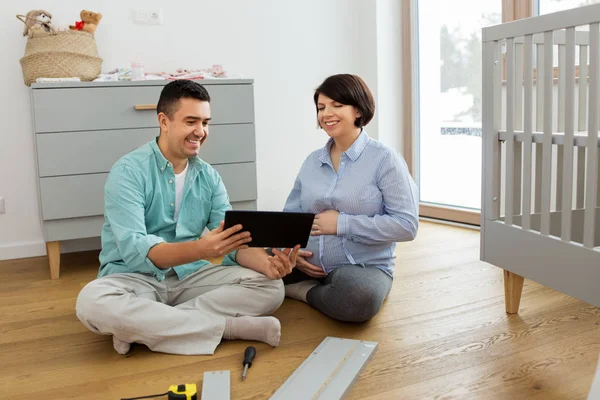 Familienpaar mit Tablet-PC baut Babybett zusammen — Stockfoto