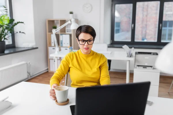 Zakenvrouw met laptop drinkt koffie op kantoor — Stockfoto
