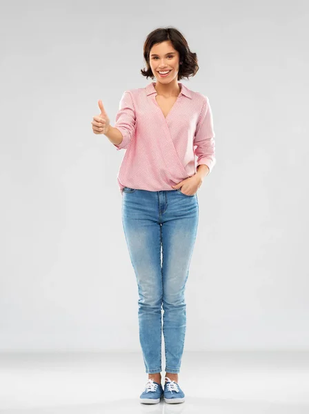 Молодая женщина в рубашке и джинсах показывает большие пальцы вверх — стоковое фото
