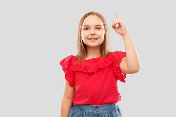 Улыбающаяся девушка в красной рубашке, указывающая пальцем вверх — стоковое фото